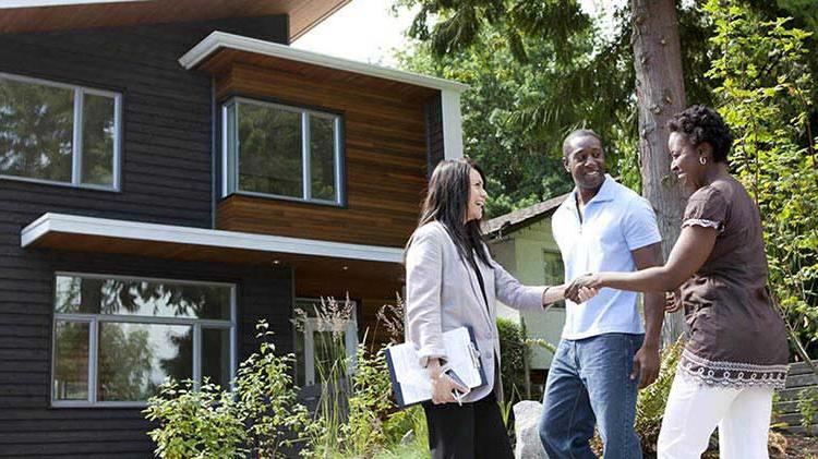  A man and a woman in front of their new house shaking hands with their realtor.