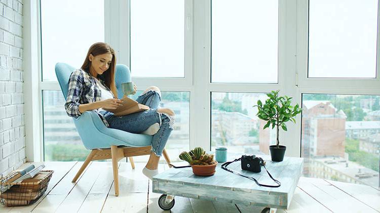 Woman reading in chair in front of window, looking happy due to buying a condo.