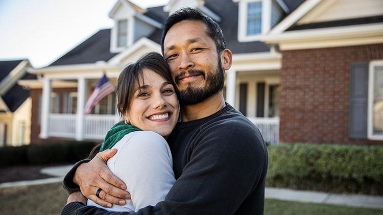 A couple embracing in front of their house.